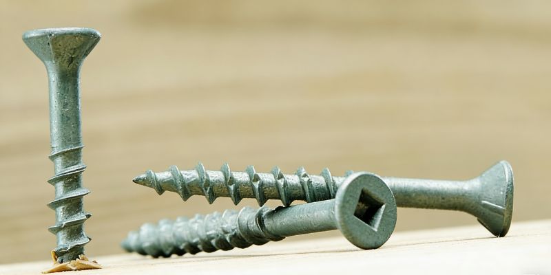 Close-up of rust-resistant green-coated wood deck screws, featuring countersunk square drive heads and sharp threads, on a light wooden surface.